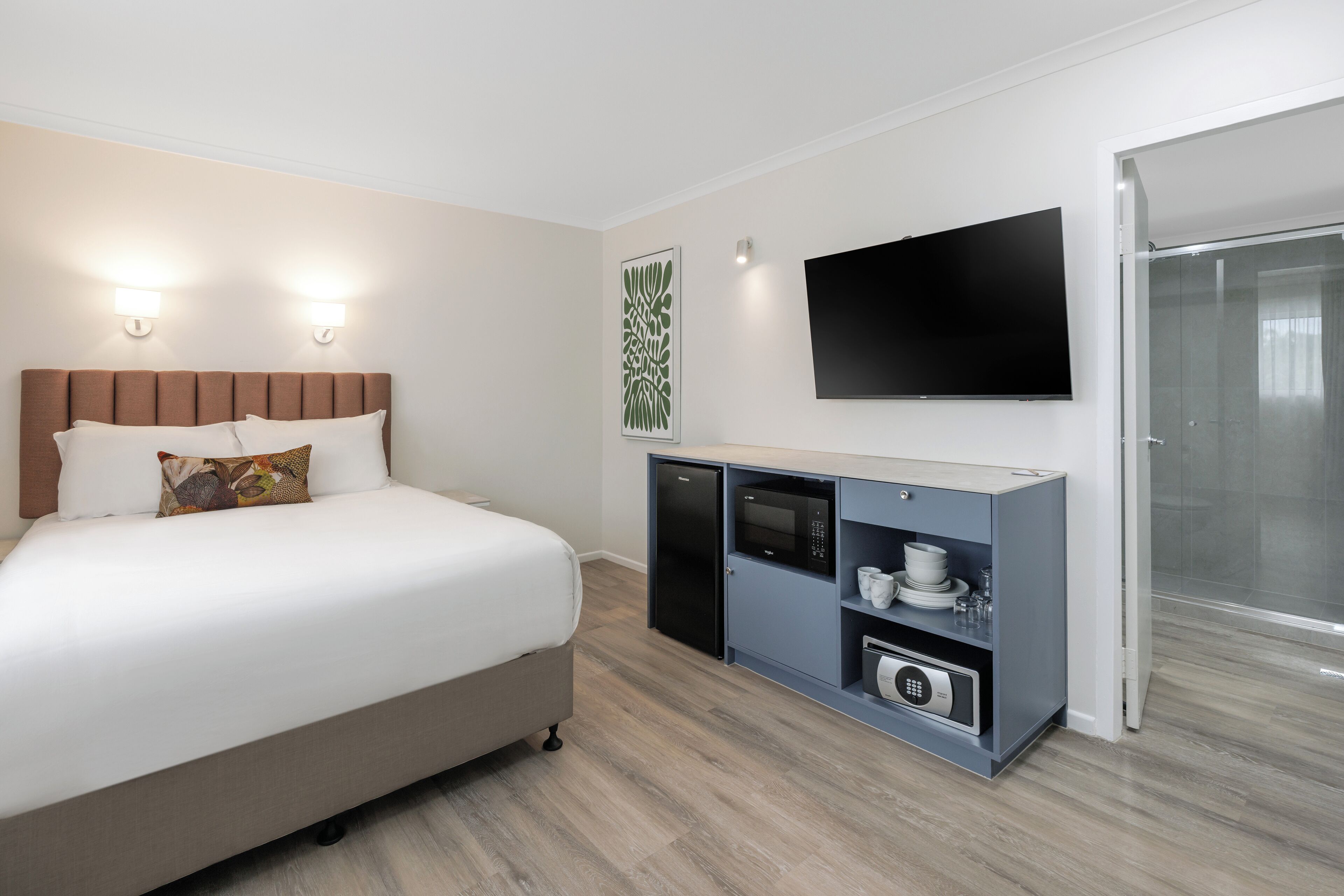 A hotel room with a bed, a minibar, a television, and a shower.
