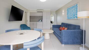 A modern living room with a blue sofa, a round dining table, and a flat-screen TV mounted on the wall.
