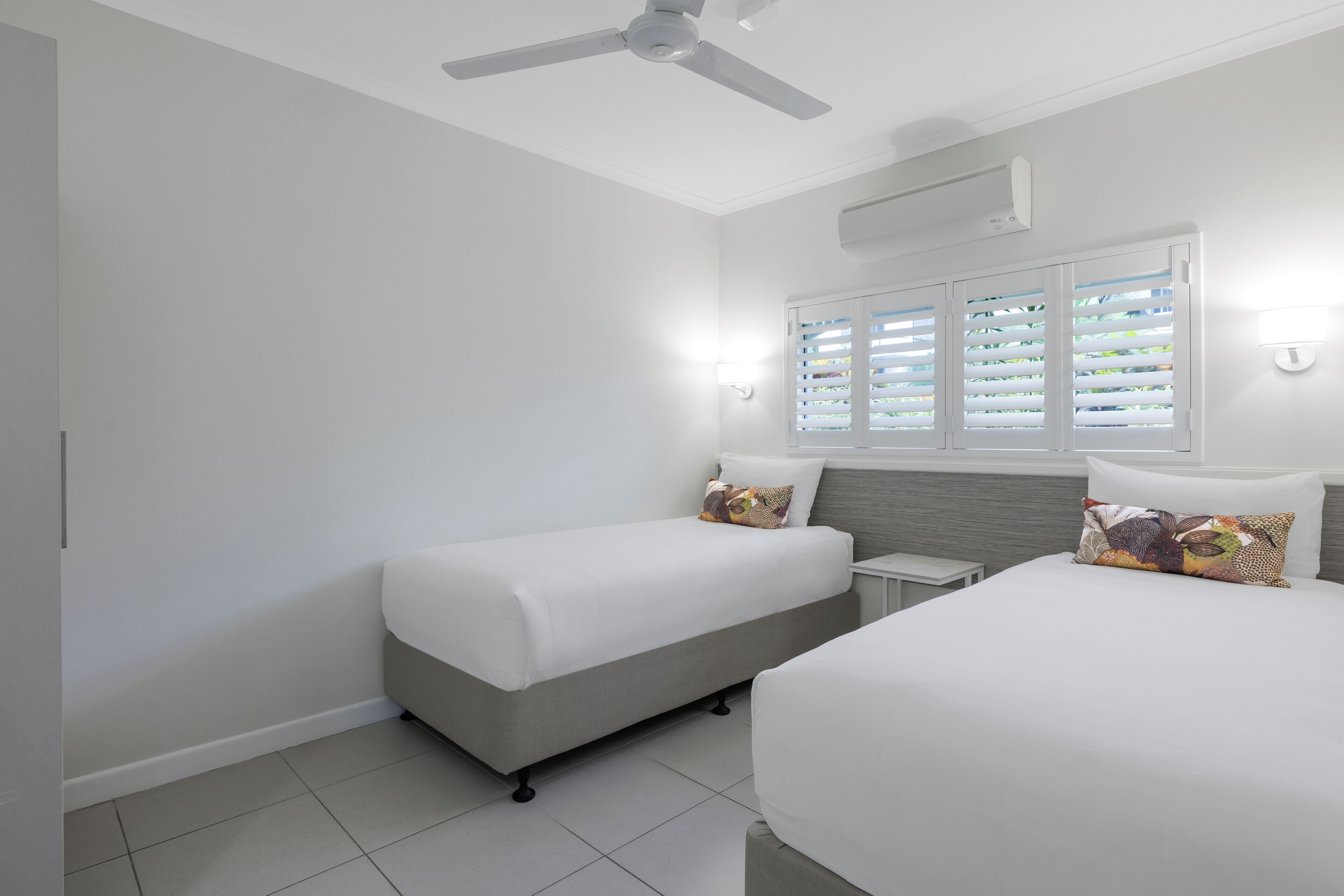 Et hotelværelse med to senge, ventilator, aircondition og et vindue med persienner.