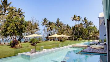 A pool area with lounge chairs and umbrellas, surrounded by palm trees and a view of the ocean.