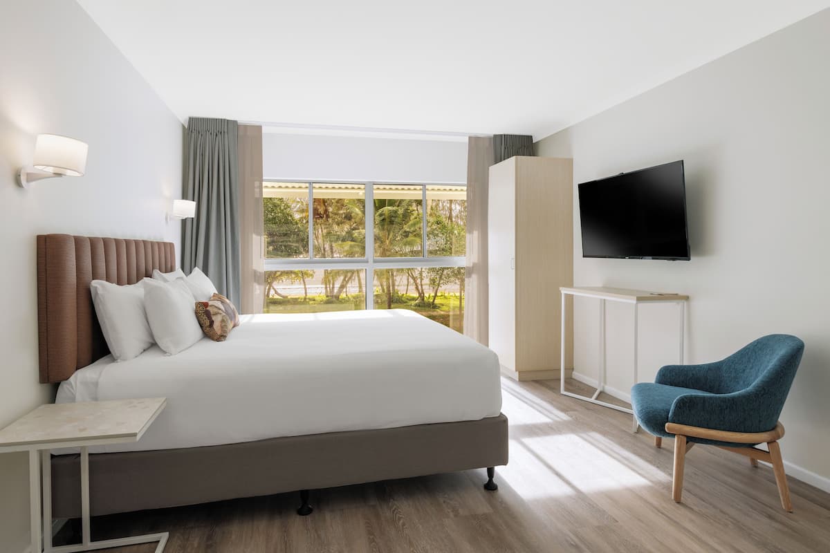 A modern hotel room with a large bed, a TV, a desk, and a chair.