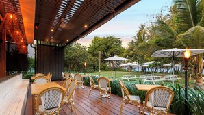 An outdoor patio with wooden tables and wicker chairs, surrounded by lush greenery and palm trees. - Club Wyndham Mission Beach (Mission Beach)