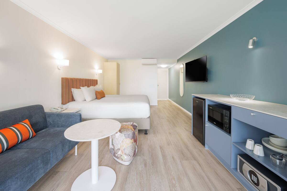 A modern hotel room with a bed, sofa, and kitchenette.