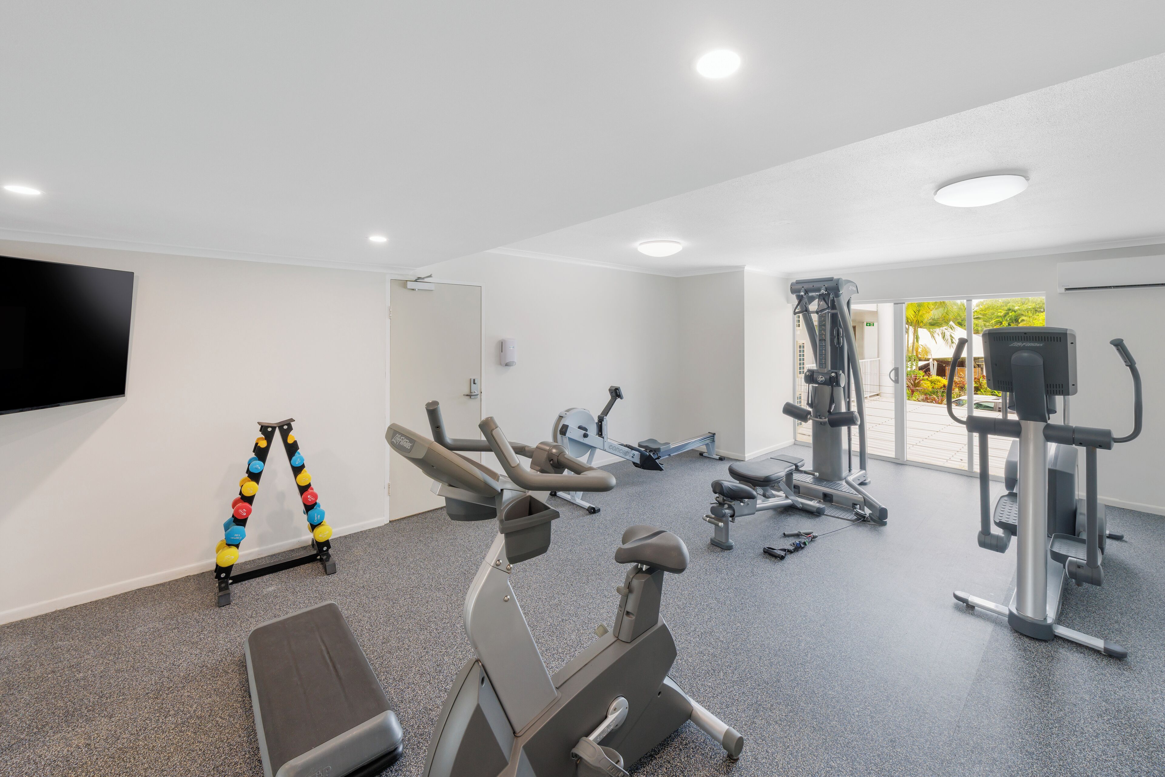 A modern gym with various exercise equipment, a bench, and a TV on the wall.