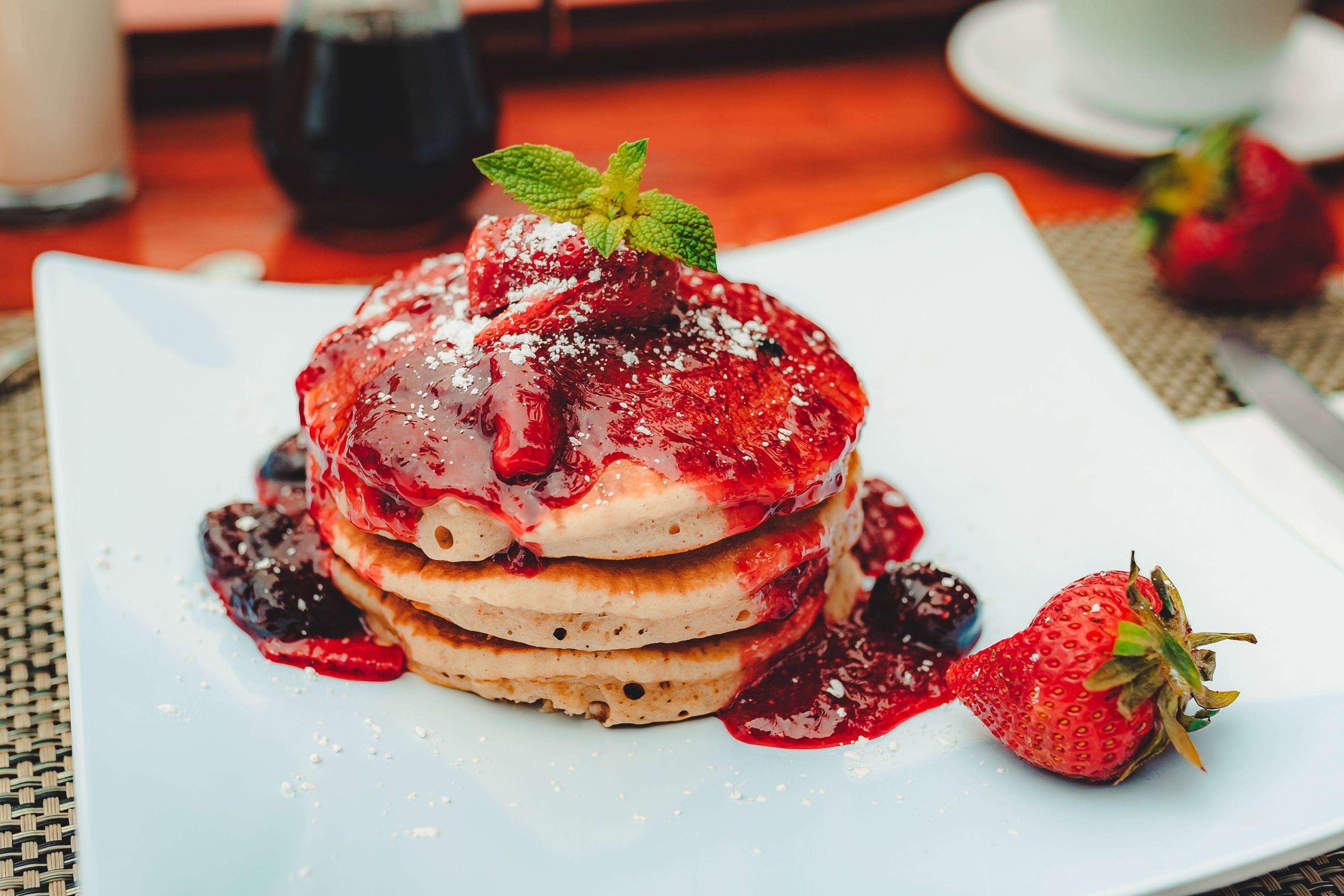 A stack of pancakes with berry compote and a strawberry on a white plate.