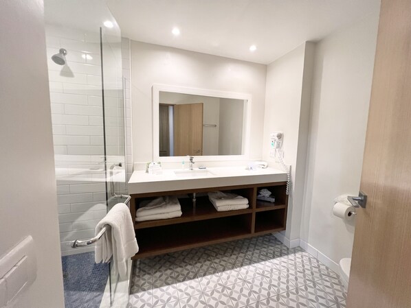 A modern bathroom with a glass shower enclosure, a white sink with a mirror above, and patterned floor tiles. - San Nicolas Hotel and Casino (Ensenada)