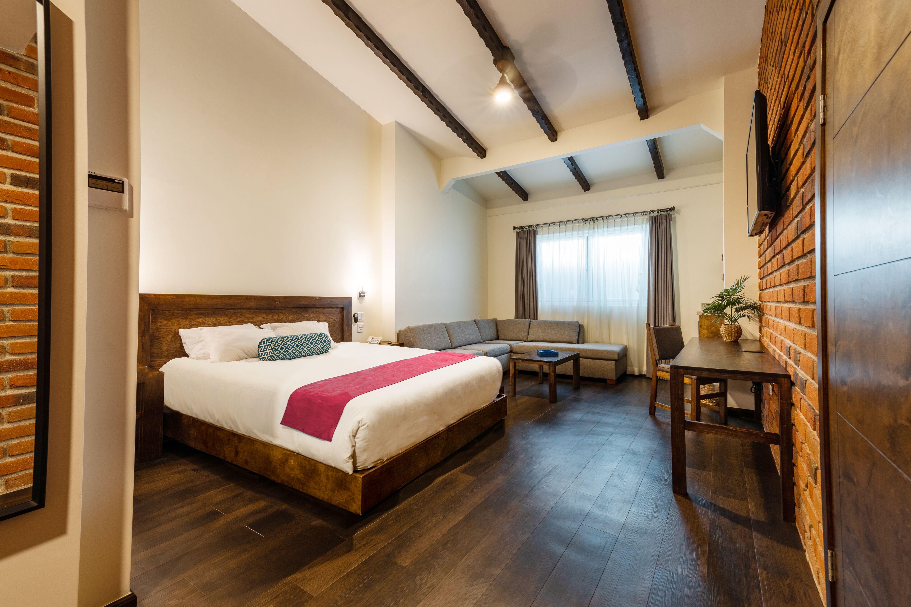 A hotel room with a large bed, a sofa, a small table, and a brick accent wall.