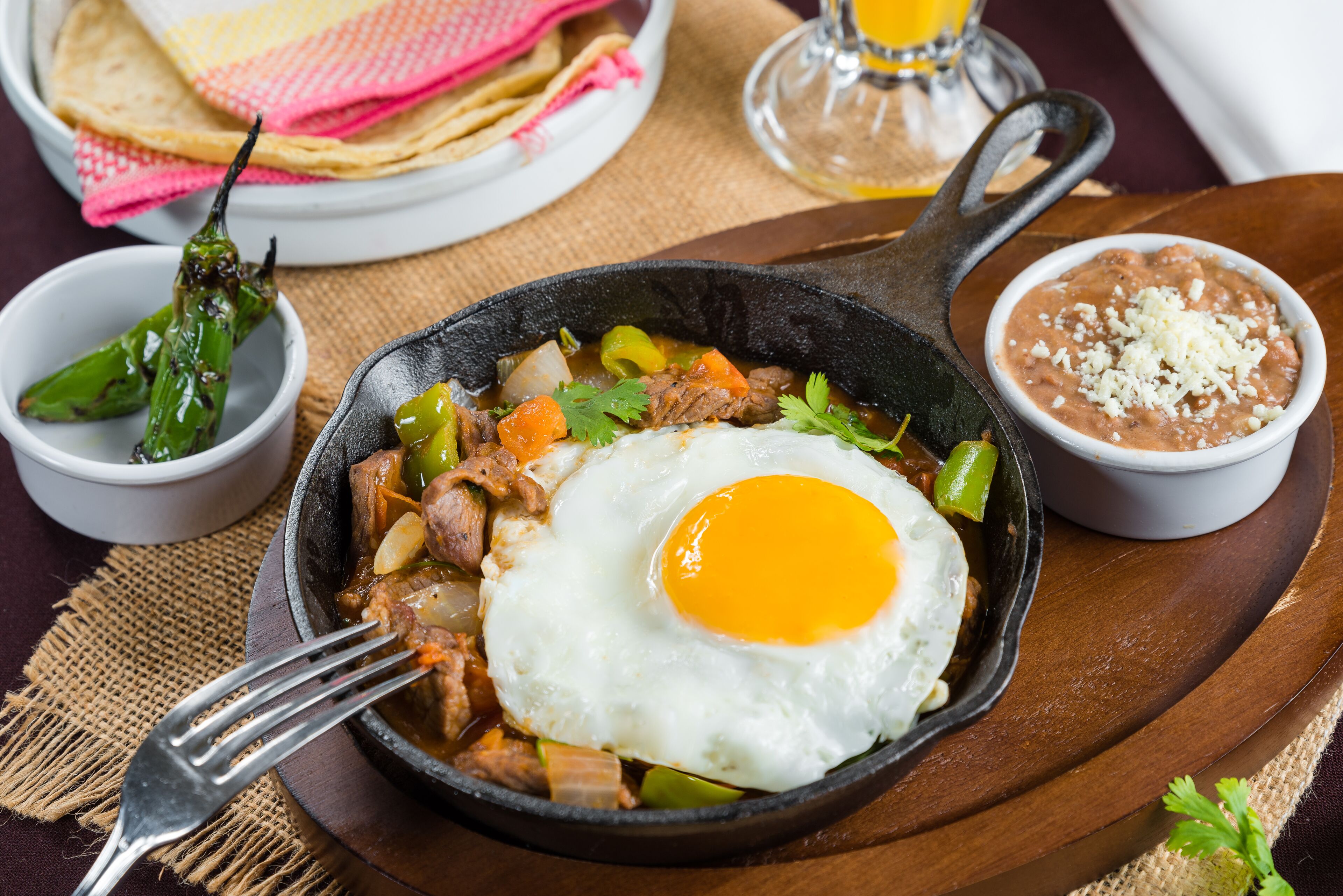 Una sartén con un huevo frito, rodeada de tazones de frijoles y un chile.