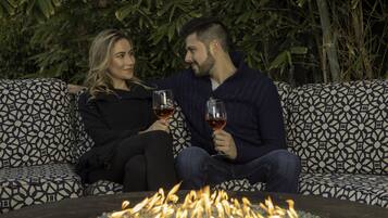 Dos personas sentadas en muebles de exterior con diseño, frente a una chimenea exterior.