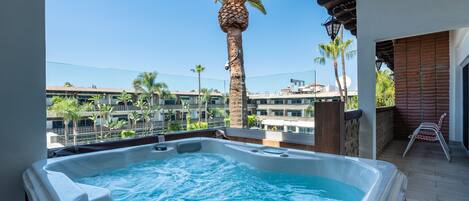 A hot tub on a balcony with a view of palm trees and buildings.