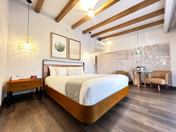 Un dormitorio moderno con una cama de madera, una mesita de noche, un escritorio y una silla. Hay cuadros enmarcados en la pared y un revestimiento de pared de ladrillo.
