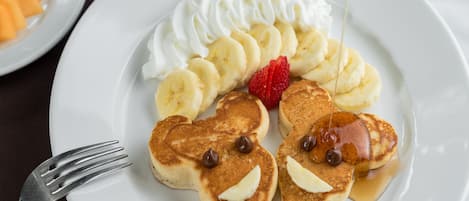 A plate of pancakes with whipped cream, bananas, strawberries, and chocolate chips.