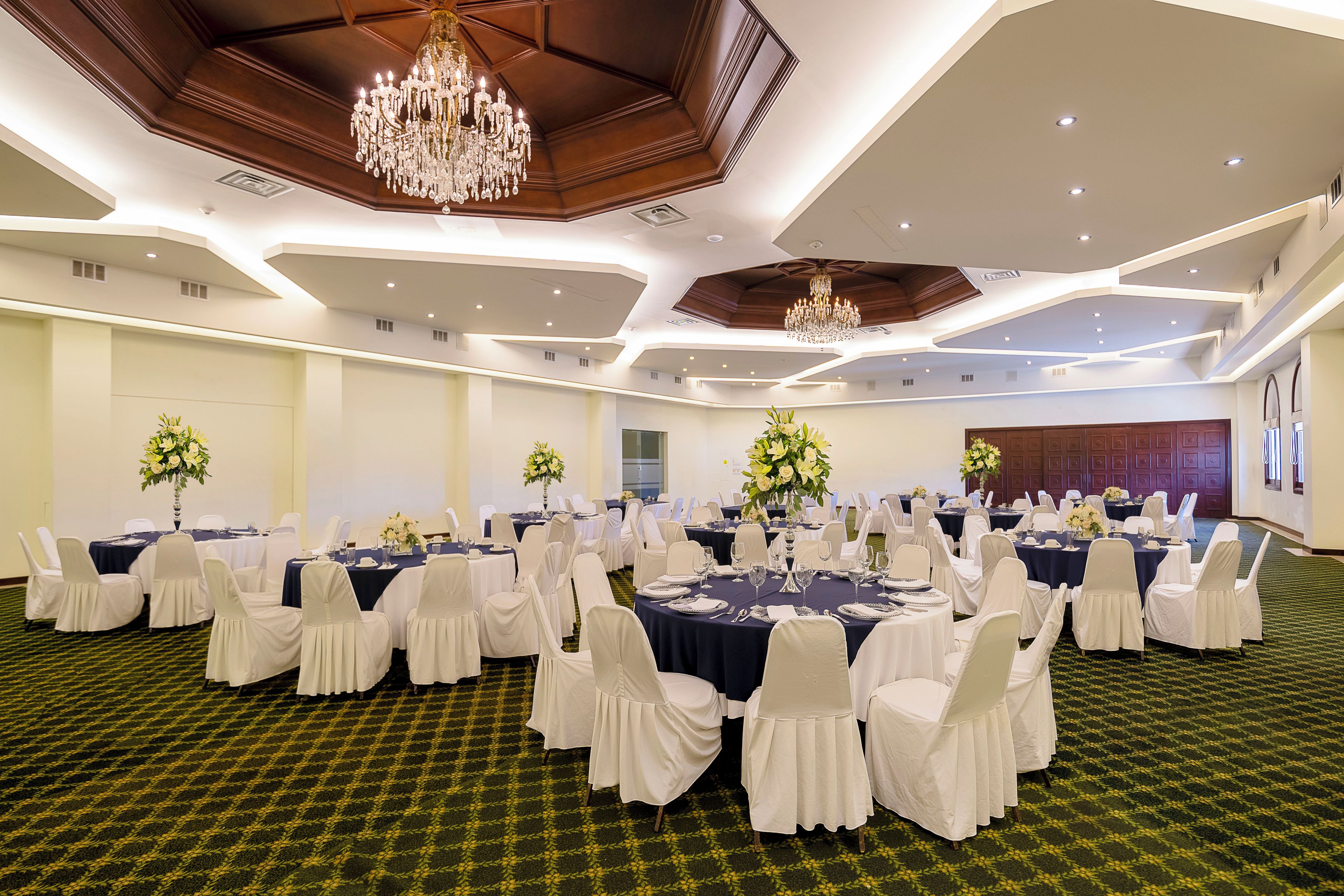 Una sala de banquet amb taules rodones, caires blancs i lustres.