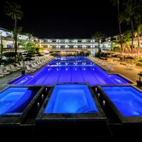 Un área de piscina con varias piscinas, sillas de descanso y sombrillas.