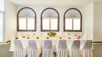 Uma sala de conferência com uma mesa comprida, cadeiras brancas e três janelas em arco.