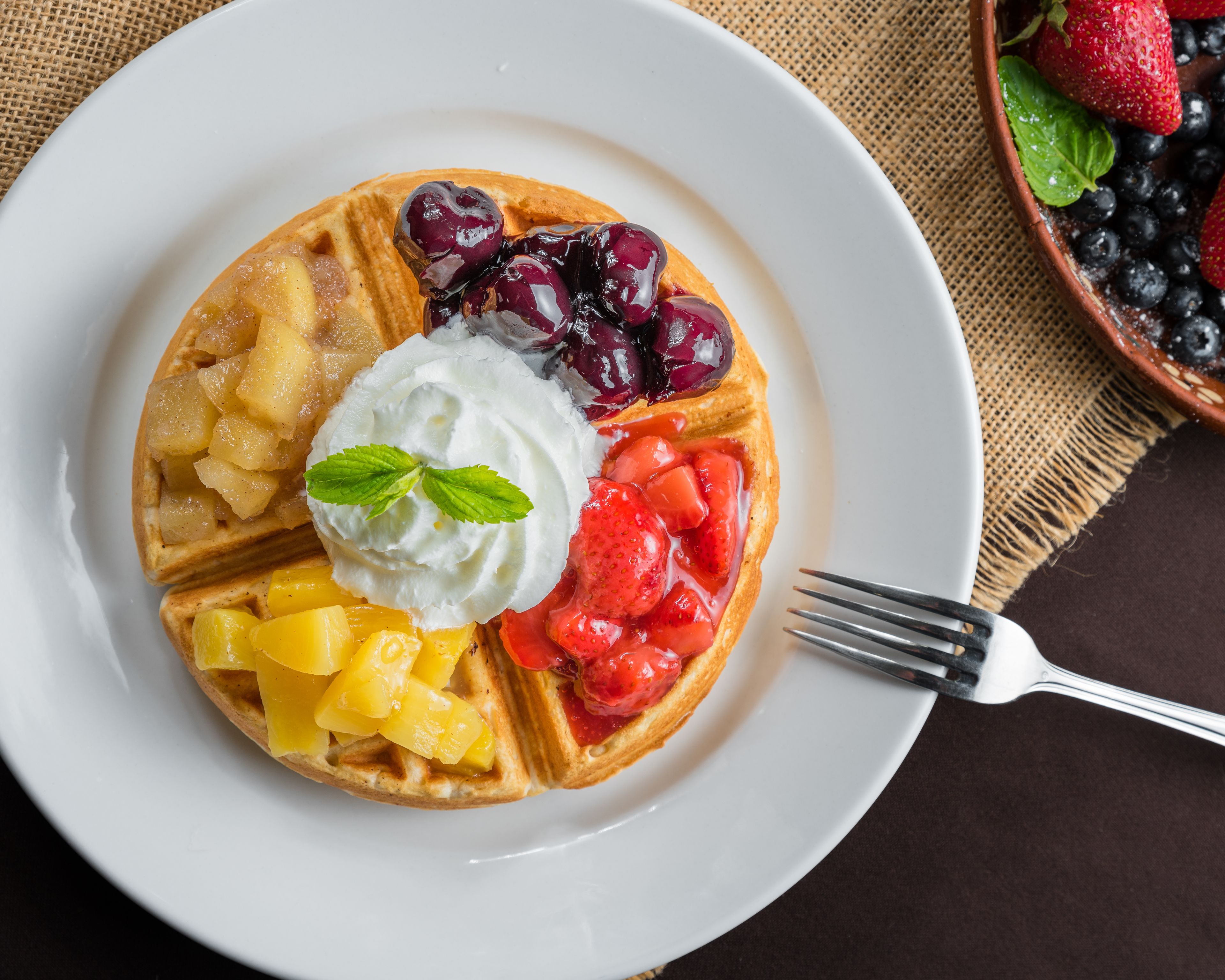 Een bord met wafelwaar, bedekt met fruit, slagroom en een muntblaadje.