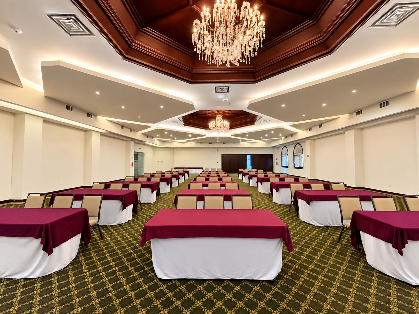 Un salón de conferencias con filas de mesas, manteles blancos y rojos, y una gran lámpara de araña.