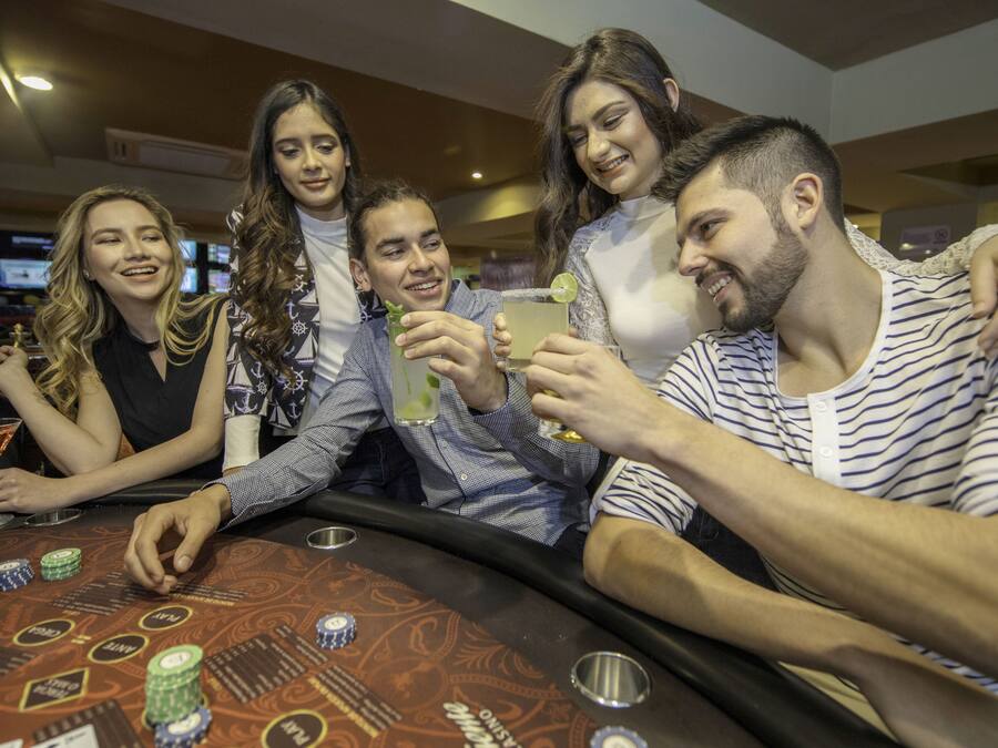 A group of people at a casino table with chips and a drink.