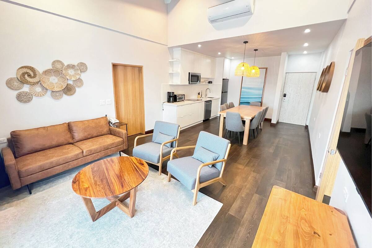 Een moderne woonkamer met een bank, twee fauteuils, een salontafel en een eethoek met een tafel en stoelen.