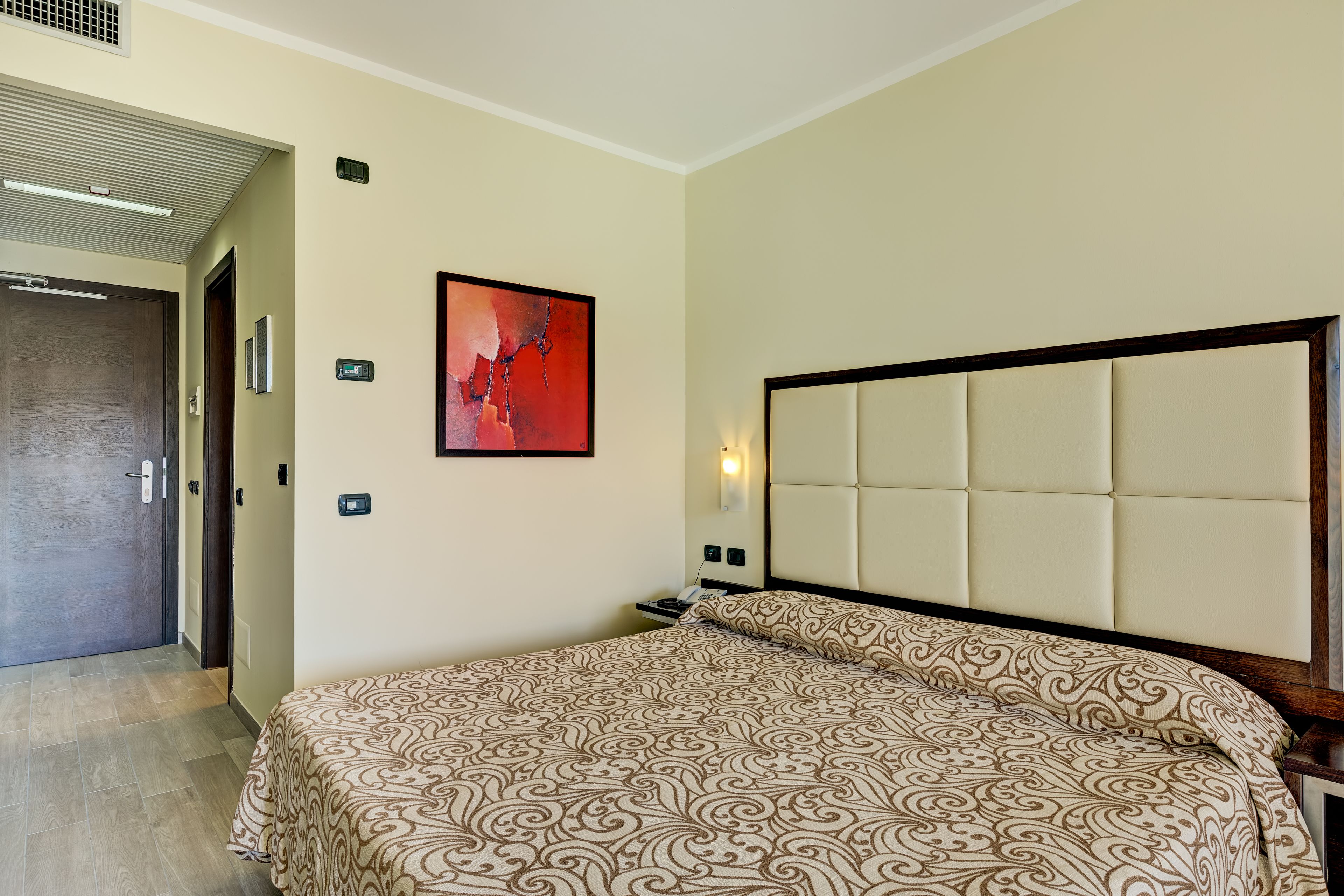 A hotel room with a large bed, a headboard, a nightstand, a wall-mounted artwork, and a door.