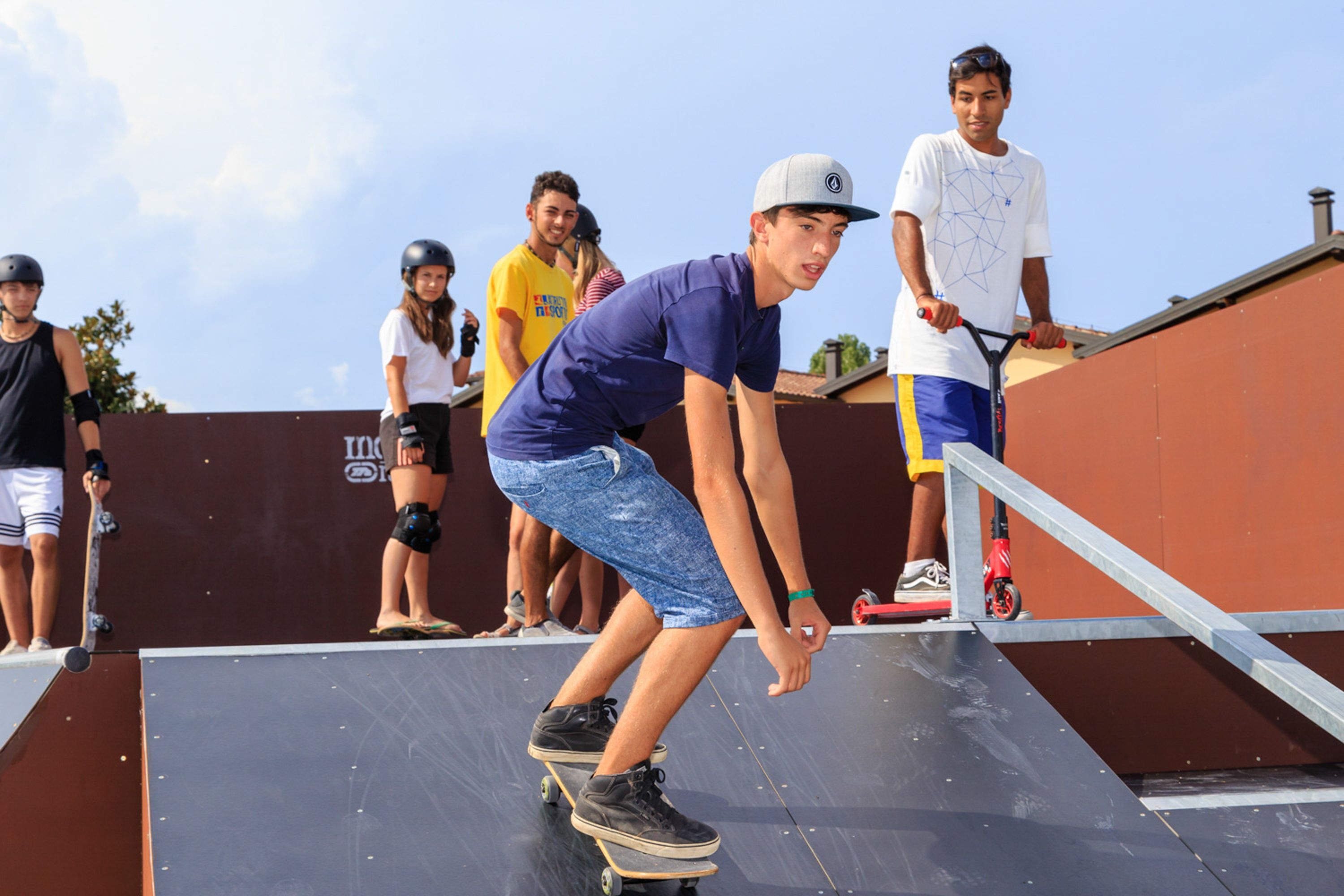 Ein Skatepark mit Sprungschanzen und einer Gruppe von Personen, einige fahren auf Skateboards, andere auf Rollern.