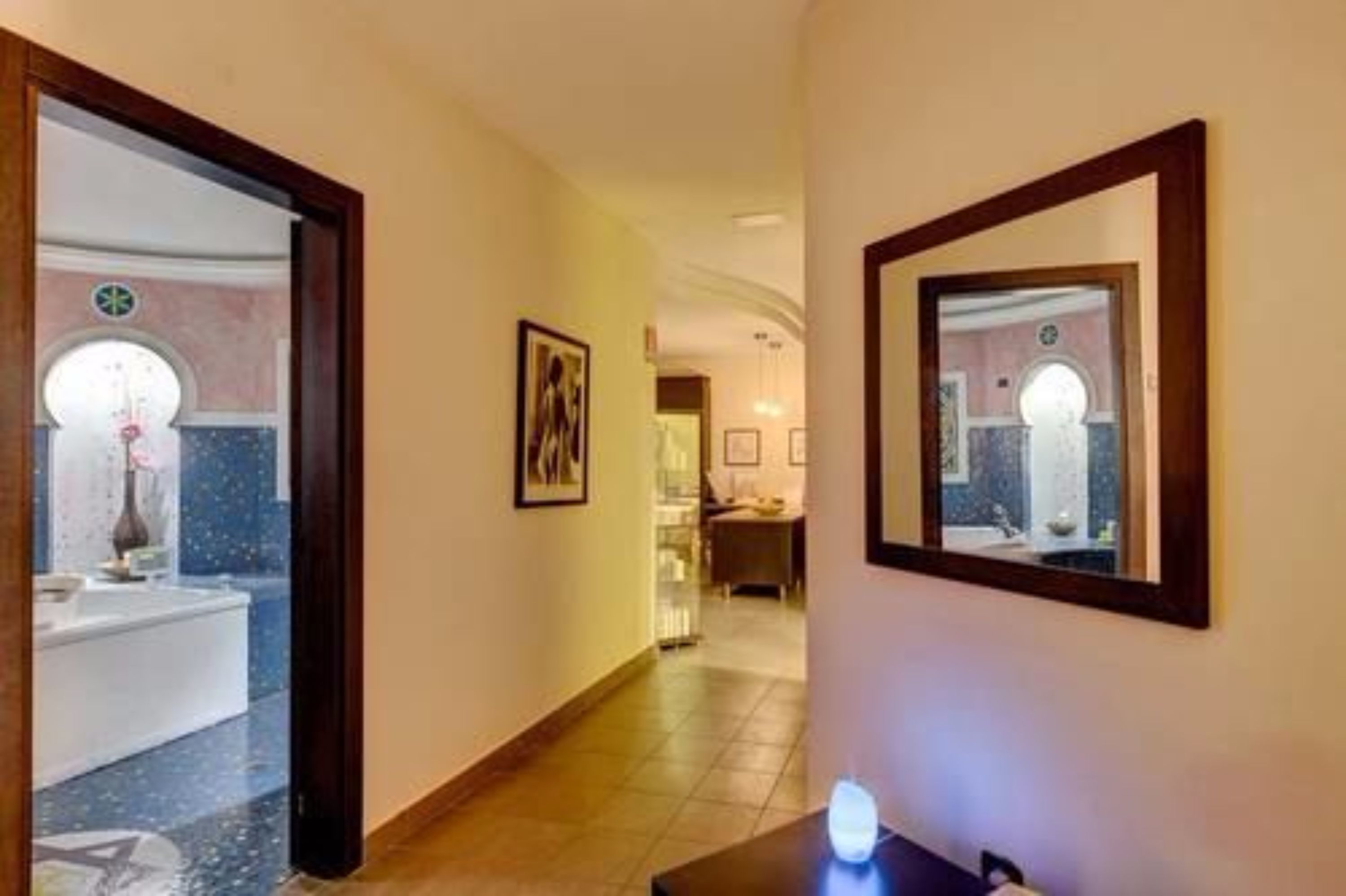 A hotel hallway with a mirror, framed artwork, and a glimpse of a bathroom with a marble floor.