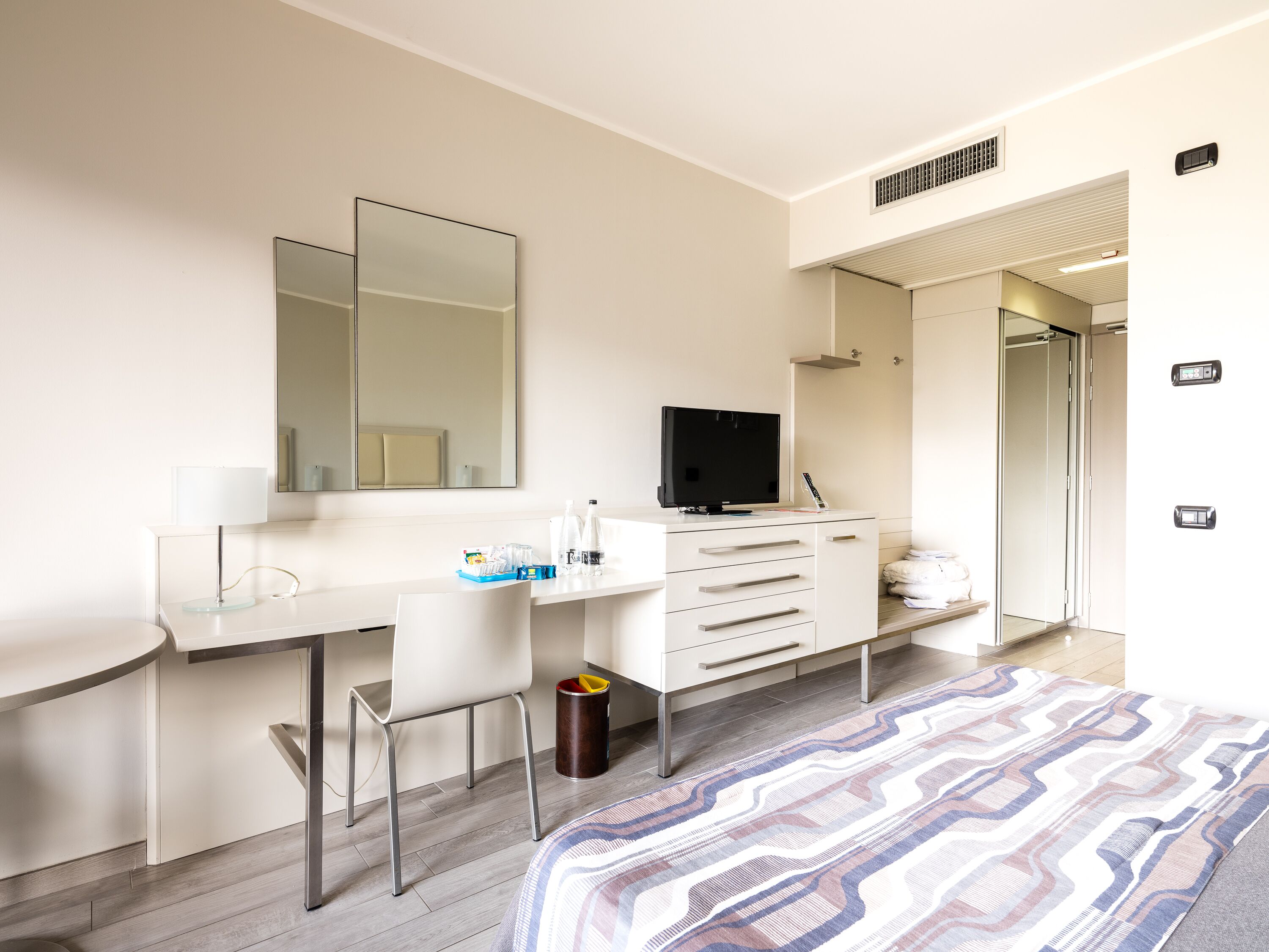 Une chambre d’hôtel moderne équipée d’un bureau, d’une chaise, d’une télévision et d’un lit avec une couvre-lit à motifs.