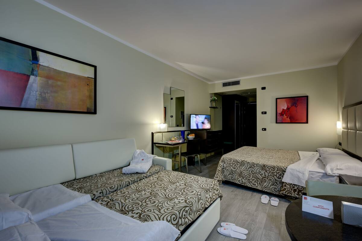 A hotel room with two beds, a desk with a computer, a TV, and a large abstract painting.