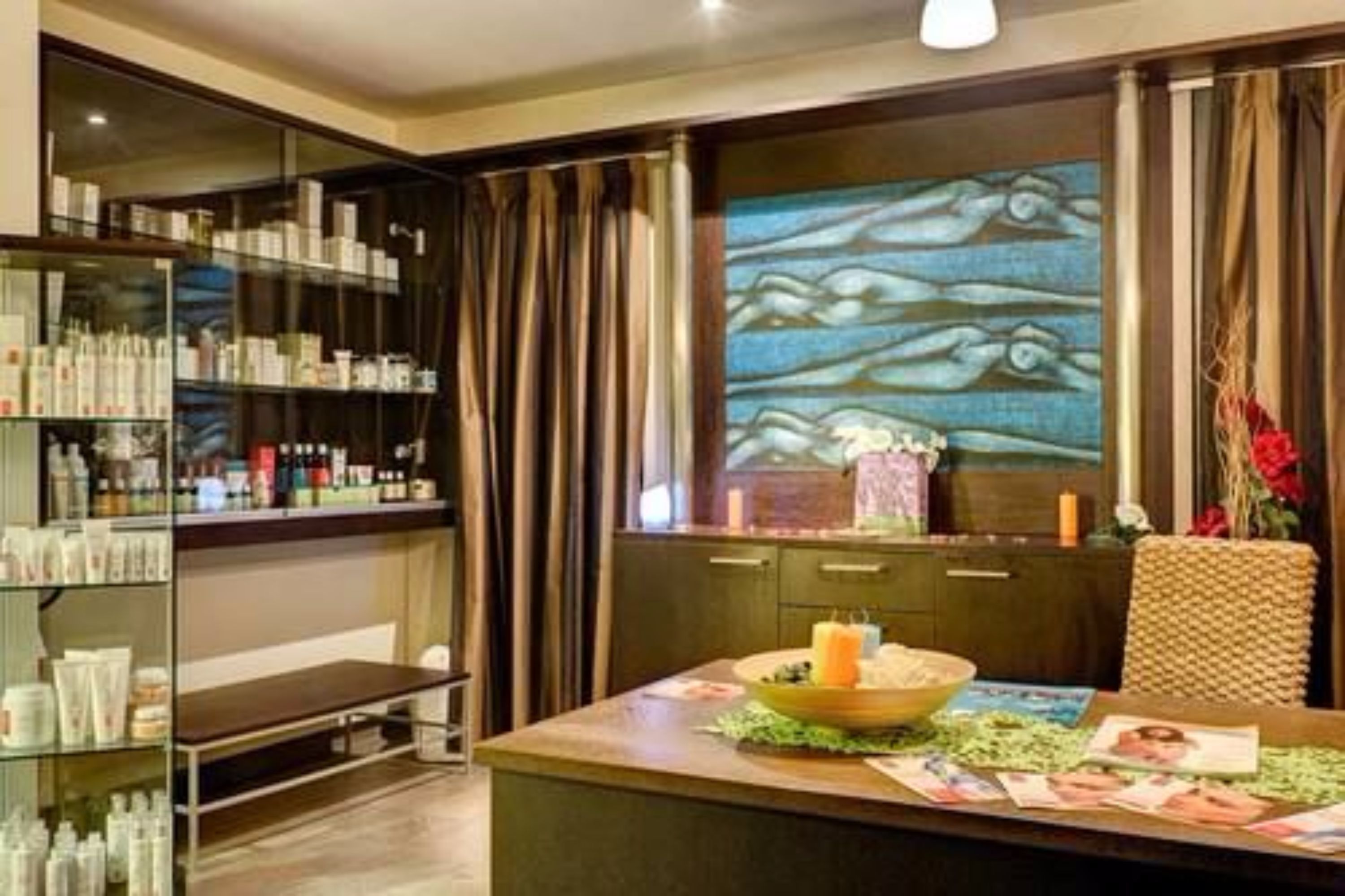 A hotel room with a large window, a bookshelf filled with toiletries, a table with a candle and magazines, and a decorative wall with a fish pattern.