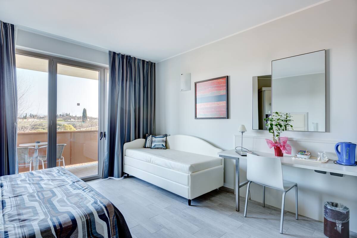 A hotel room with a bed, a sofa, a desk, and a large window with curtains.