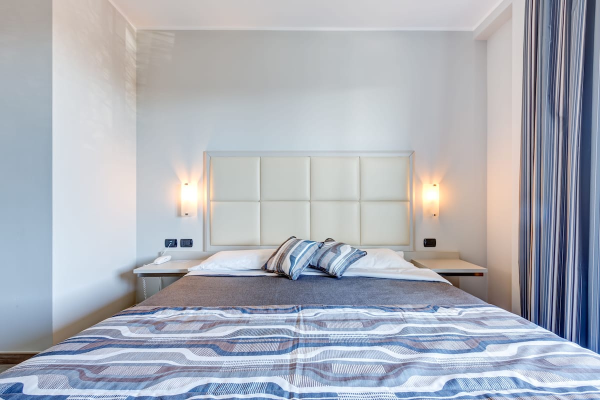 A hotel room with a large bed, two bedside tables, a headboard, and wall-mounted lights.