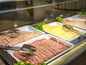 Un bufé con diversos alimentos, incluyendo carnes y quesos en rebanadas.