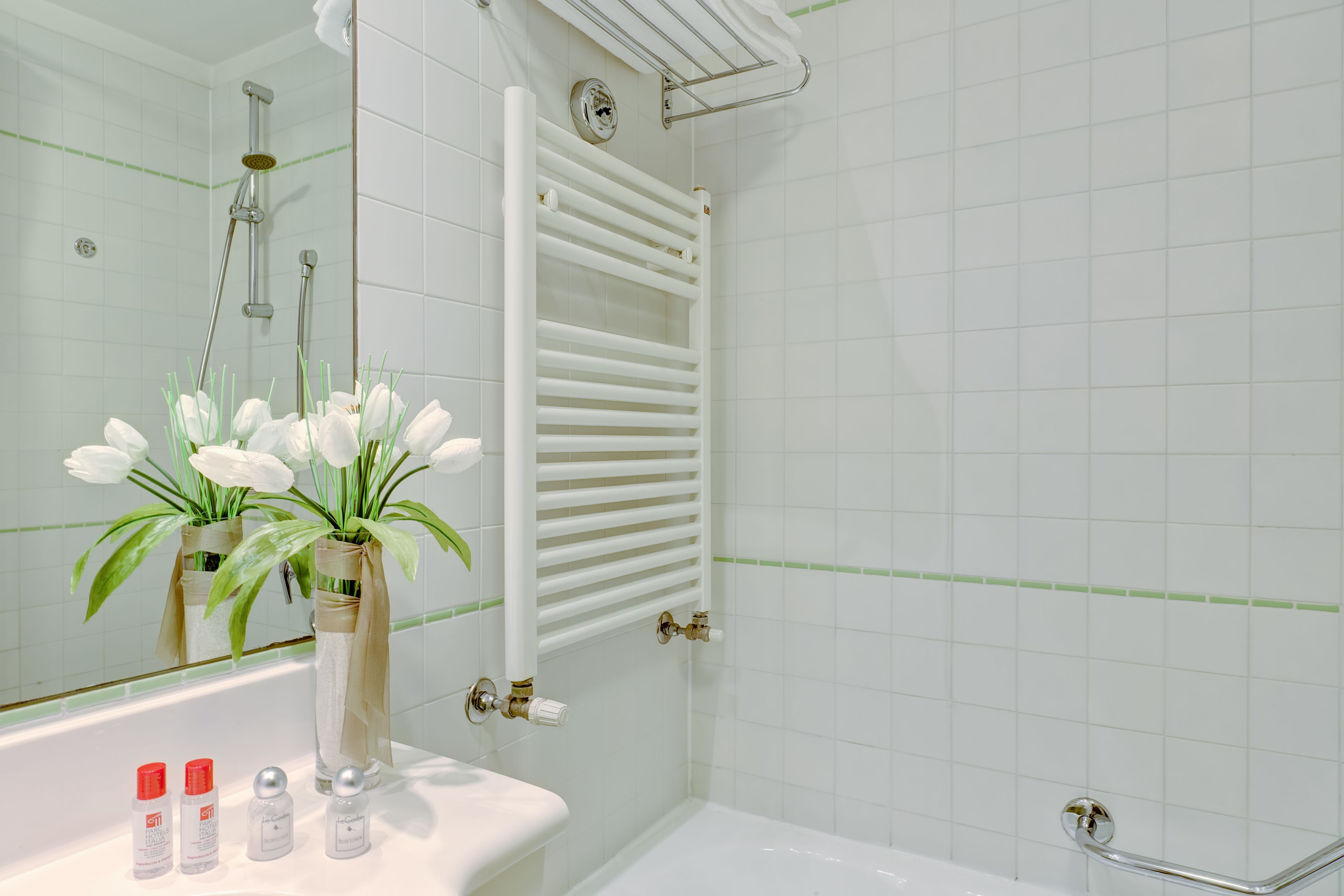 Un baño con una bañera blanca, un toallero blanco y un espejo que refleja la zona de la ducha.