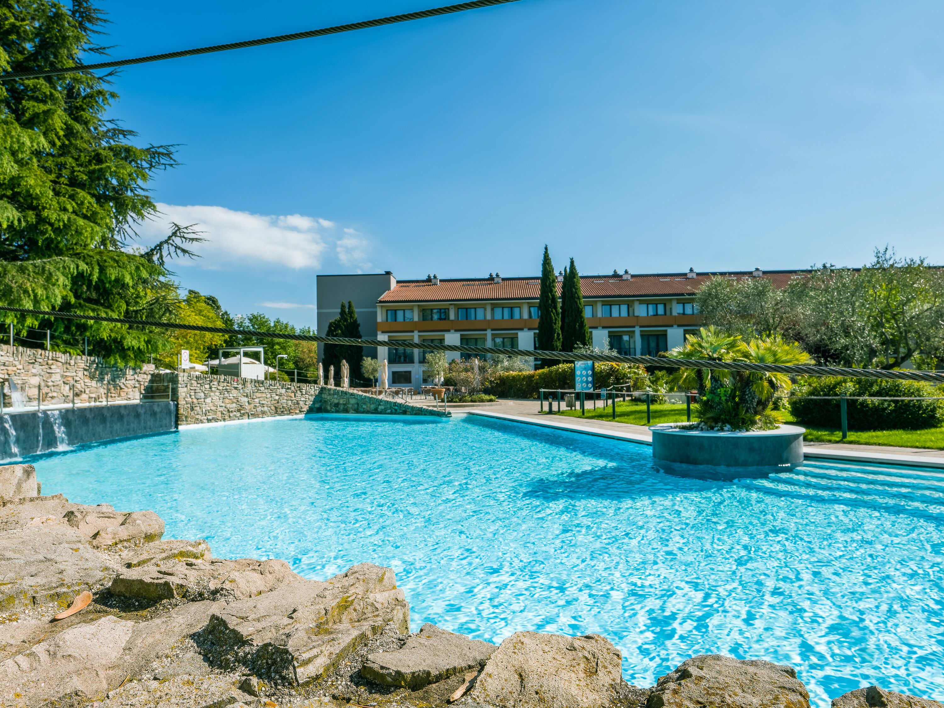 A clear blue pool with a stone wall and a building in the background.
