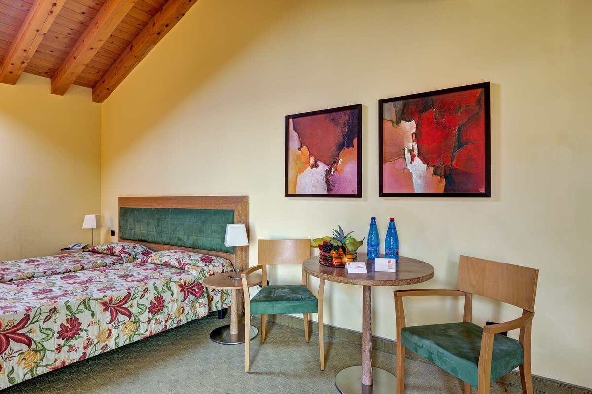 A hotel room with two beds, a round table with chairs, and artwork on the wall.