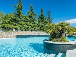 Una piscina azul cristalina rodeada de muros de piedra y exuberante vegetación, incluyendo árboles altos y una palmera.