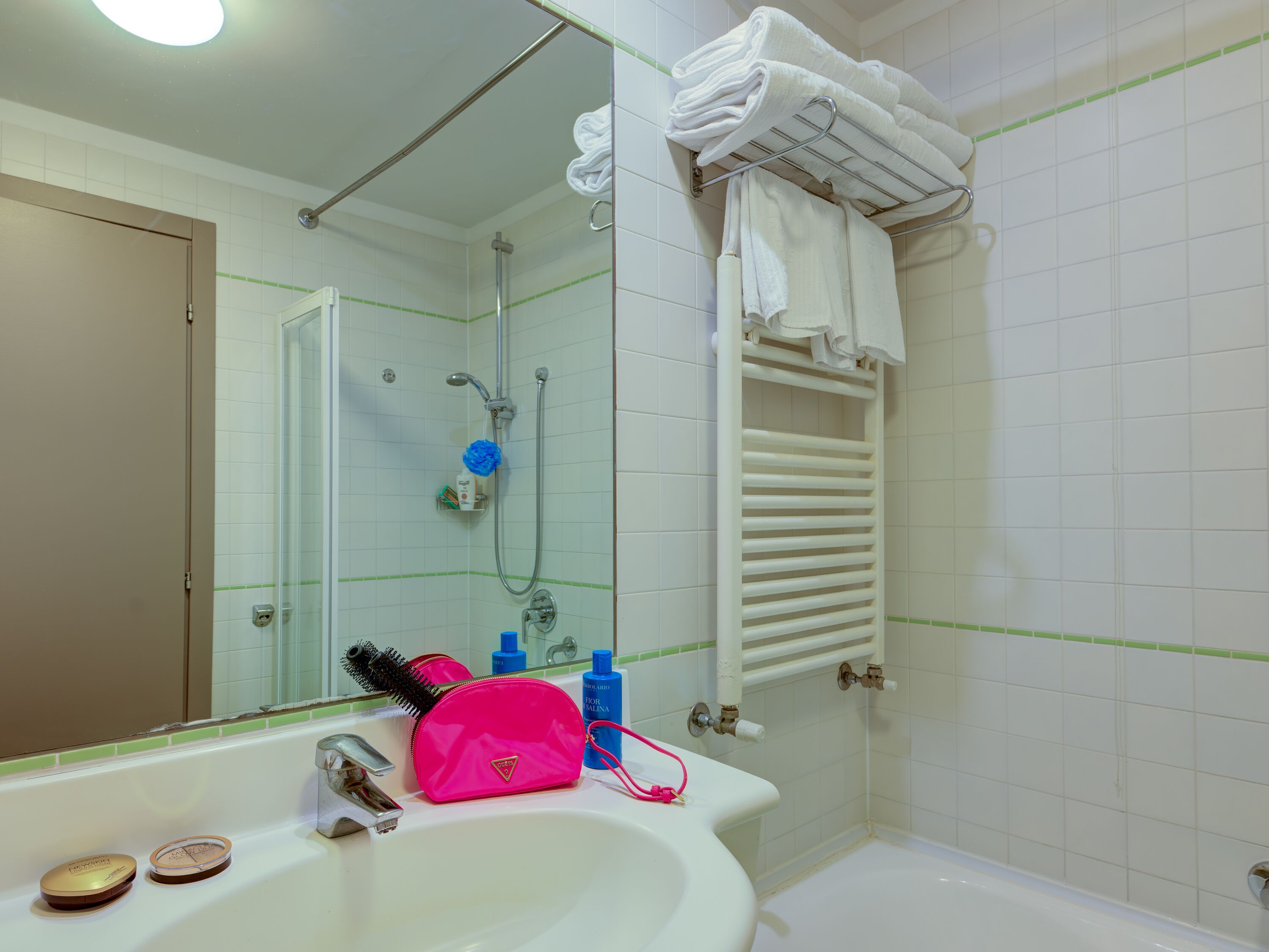 Uma casa de banho com uma pia branca, espelho, chuveiro e um porta-toalhas.