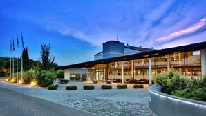 A modern hotel with a glass facade, outdoor seating area, and landscaped garden. - Parc Hotel (Castelnuovo del Garda)