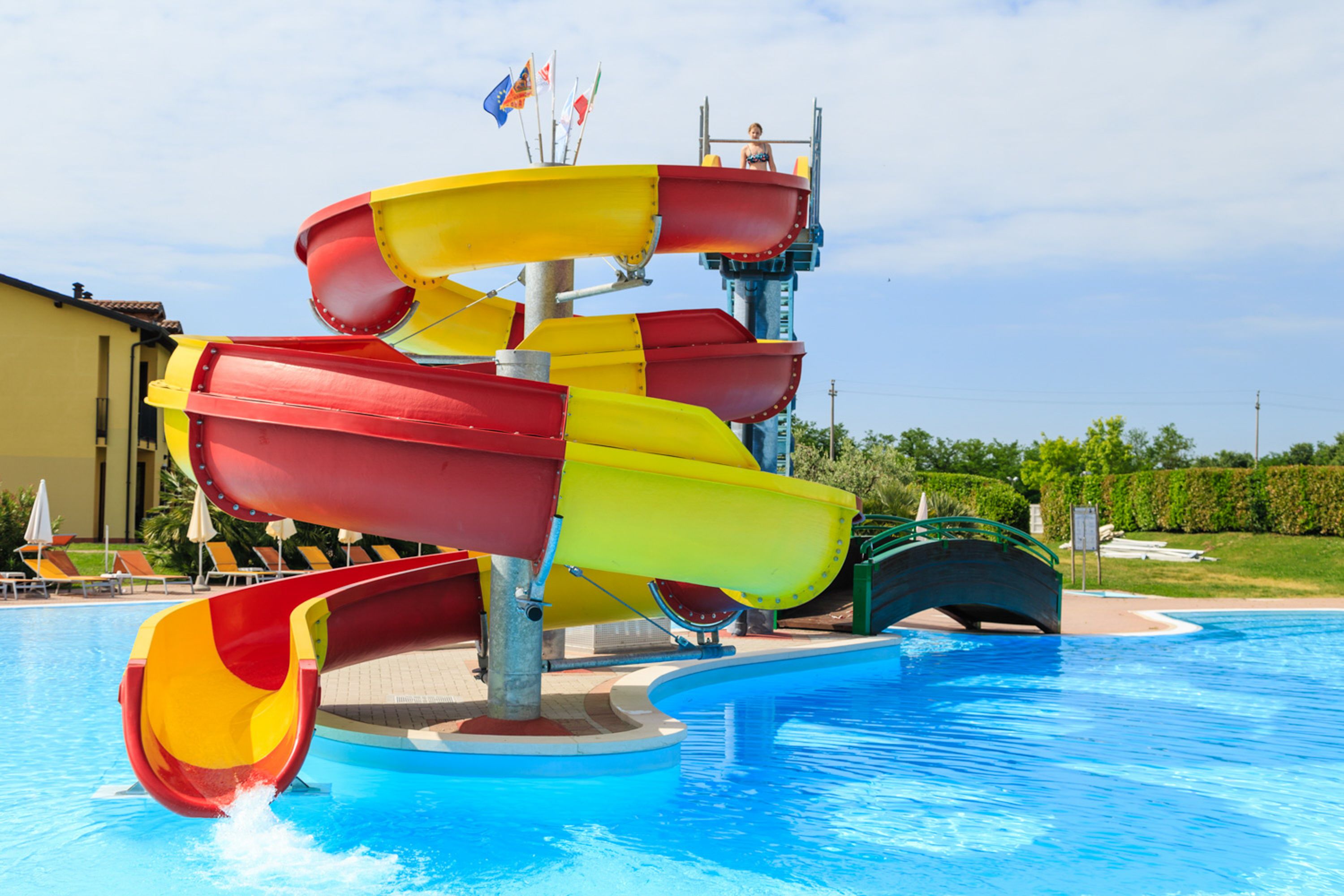 A multi-level water slide with red and yellow sections, a pool, and a bridge.