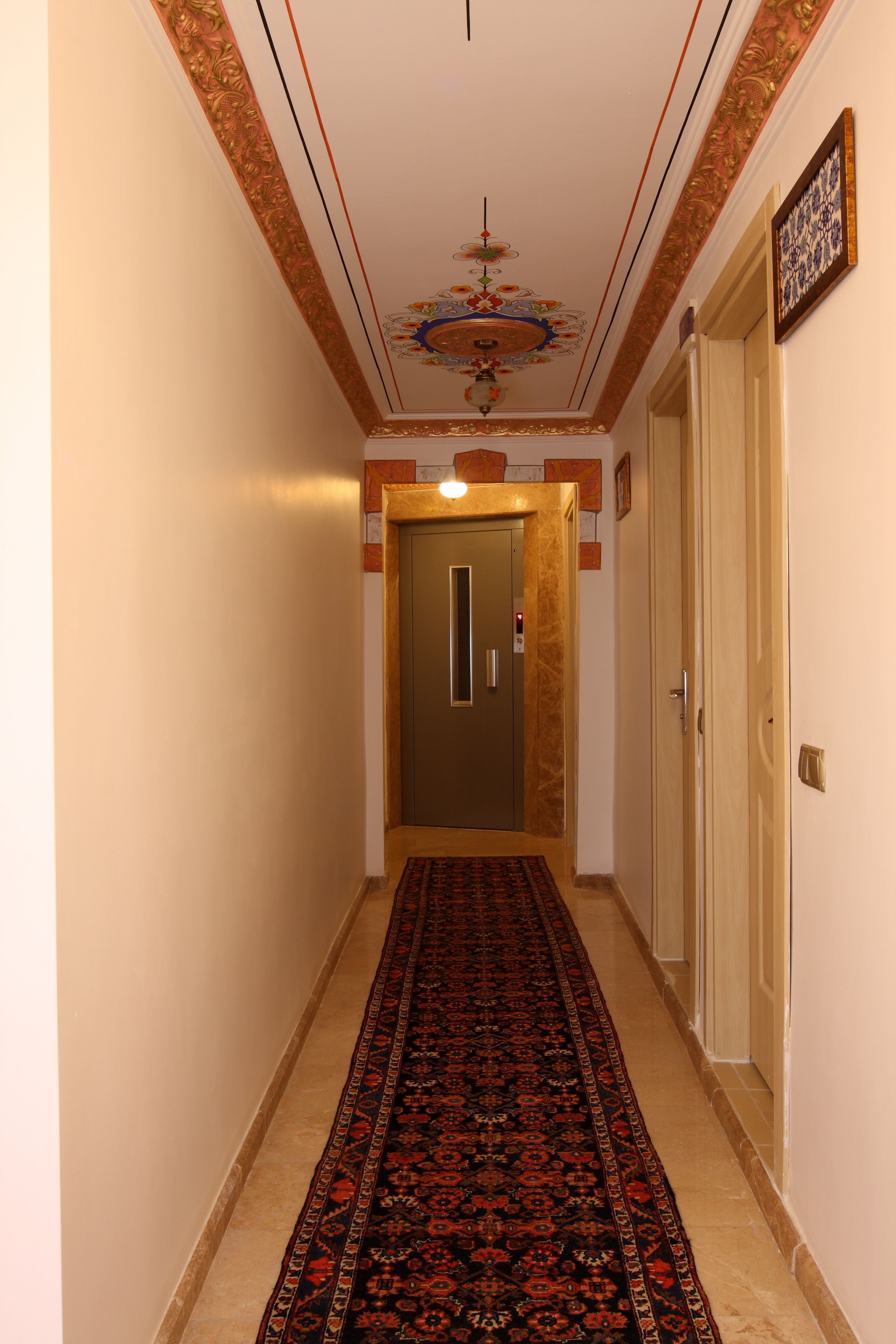 Ein Korridor mit einem gemusterten Teppich, einer verzierten Decke und einer Tür am Ende.
