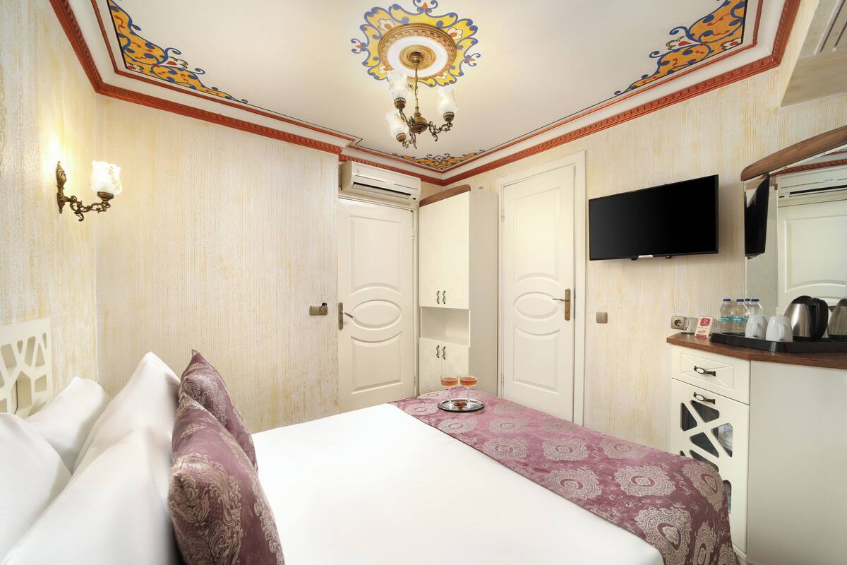 A hotel room with a bed, a television, a minibar, and a ceiling with decorative patterns.