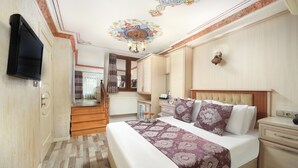 Habitació d'hotel amb un llit gran, televisió, un candelabrum i vista de la cuina i el passadís.