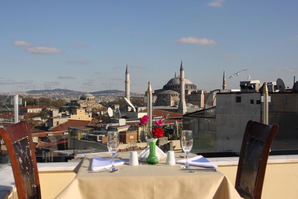 A table set for two with a view of a cityscape, including a prominent mosque with two minarets and a dome.