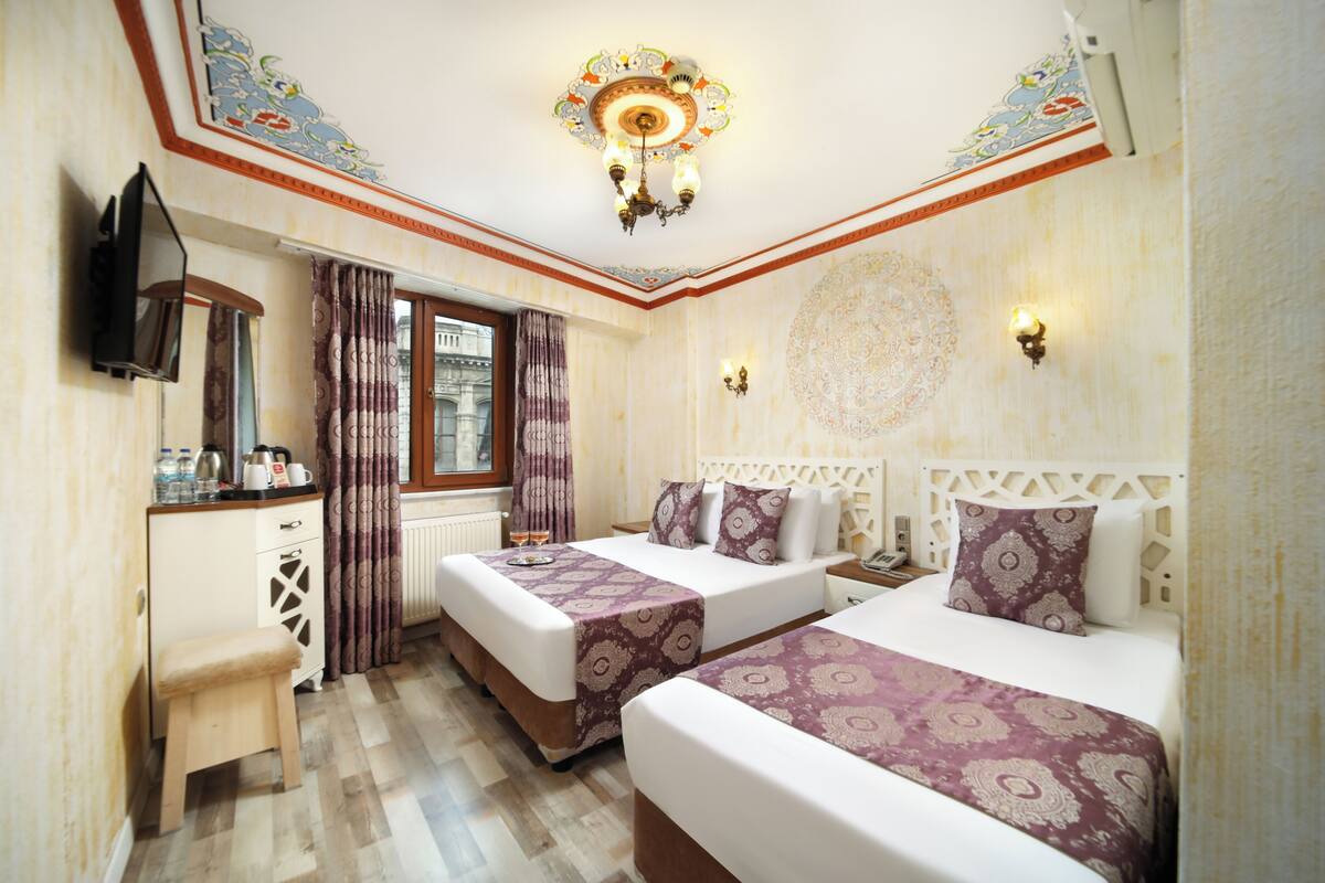 A hotel room with two beds, a desk, a TV, and a window with curtains.