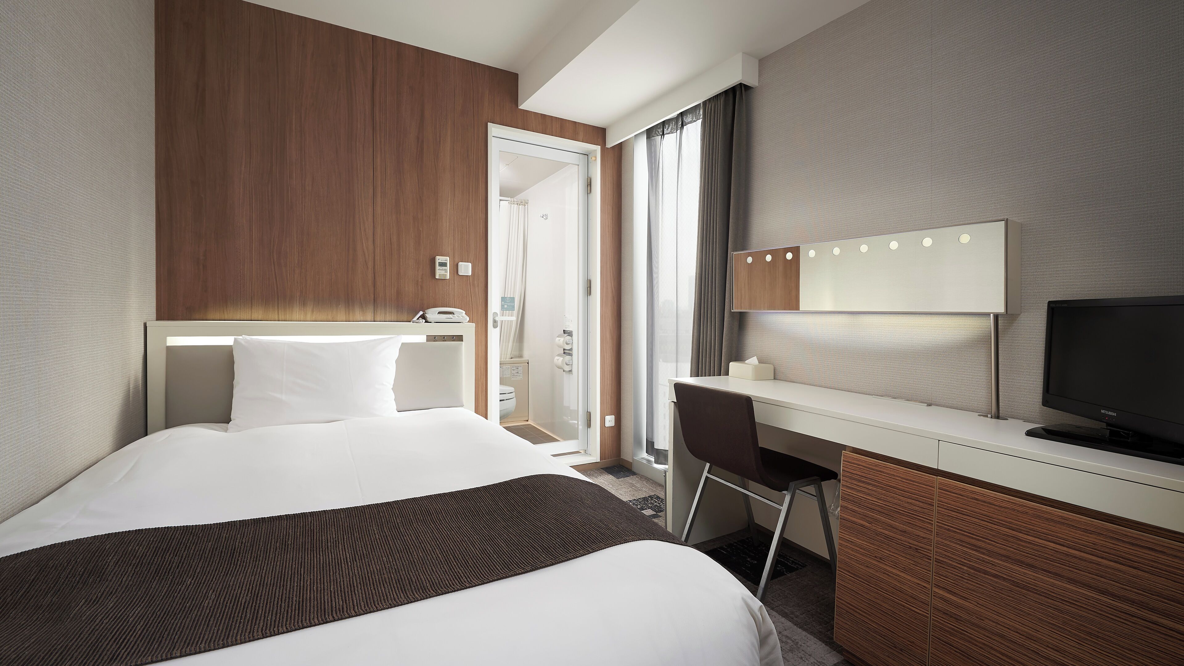 Une chambre d’hôtel avec un lit, un bureau, une télévision et une salle de bain visible à travers une porte ouverte.