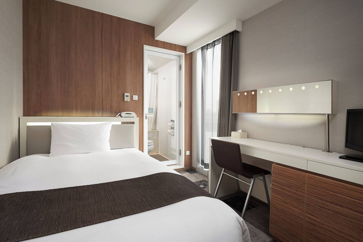 Une chambre d’hôtel avec un lit, un bureau, une télévision et une salle de bain visible à travers une porte ouverte.