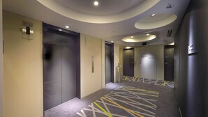 A modern hotel corridor with elevators, a patterned carpet, and recessed lighting. - Sotetsu Fresa Inn Shimbashi-Karasumoriguchi (Tokyo)