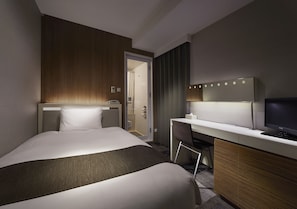 A hotel room with a bed, a desk, a television, and a bathroom visible through an open door.