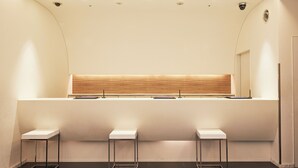 A modern reception area with a wooden counter, three white stools, and recessed ceiling lights. - Sotetsu Fresa Inn Shimbashi-Karasumoriguchi (Tokyo)