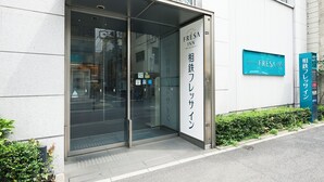 A hotel entrance with a glass door, a signboard with the hotel name, and a small garden area. - Sotetsu Fresa Inn Shimbashi-Karasumoriguchi (Tokyo)